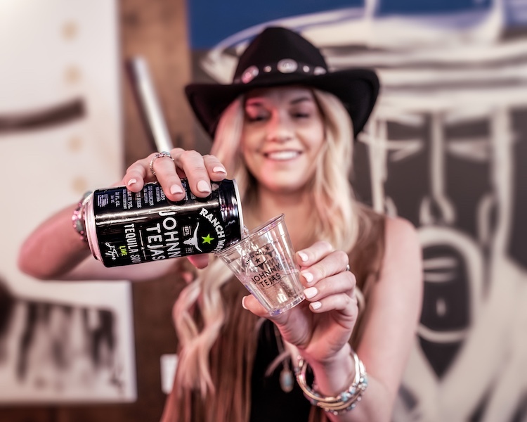 Woman pouring Johnny Tejas Tequila Lime Ranch Water into a branded cup at a Western-themed event.